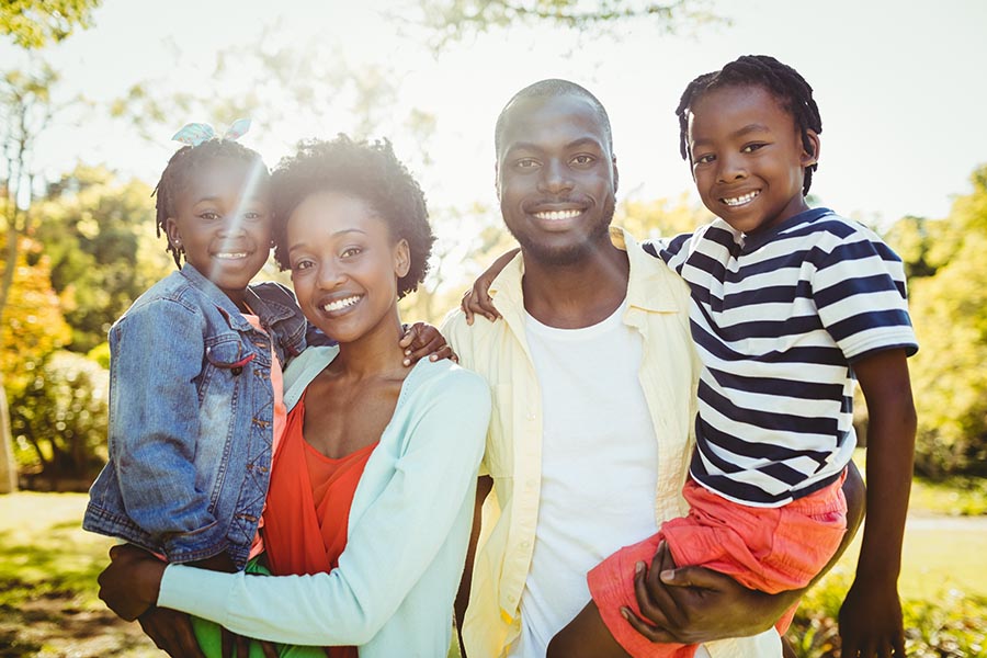 Personal Insurance - Mother and Father Hold Their Two Young Kids, Smiling and Standing Together in Their Backyard