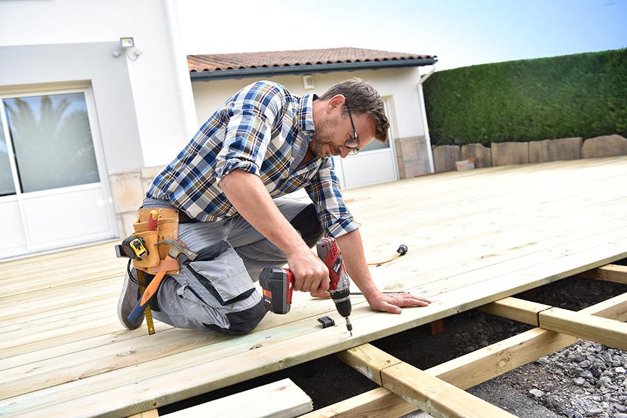 Specialized Business Insurance - Contractor in Jeans and Flannel Builds a Deck Onto a Home on a Sunny Day